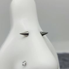 a white mannequin head with two silver spikes on it's face and one diamond in the middle