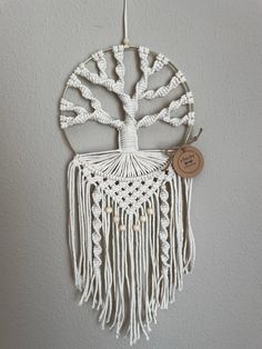 a white macrame hanging on the wall with a wooden disc attached to it