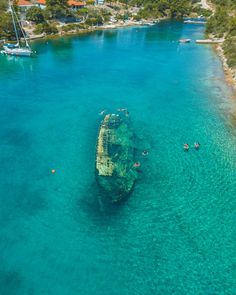 an old boat is in the middle of clear blue water with people swimming around it