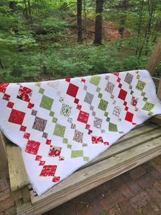 a quilted blanket sitting on top of a wooden bench in the middle of a forest