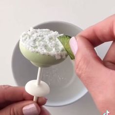 a person is holding a small green drink with whipped cream on top and a lime slice sticking out of it