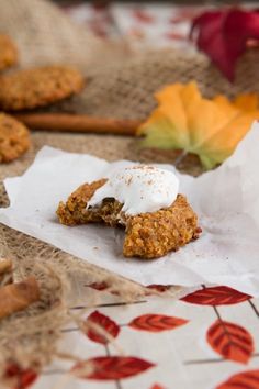 two cookies with white frosting on top and some leaves in the background, one is half eaten