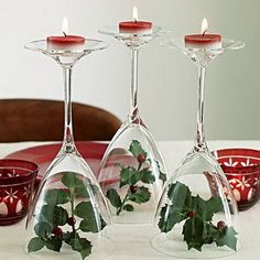 three wine glasses with holly and candles in them