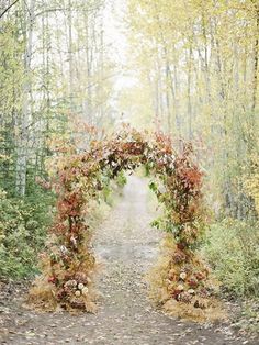 an arch made out of hay and flowers in the middle of a dirt road surrounded by trees