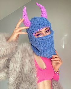 a woman wearing a knitted blue and pink mask with purple horns on her head