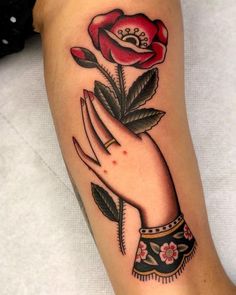 a woman's hand holding a rose tattoo on her left arm, with leaves and flowers in the middle