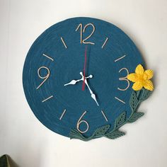 a blue wall clock with yellow flowers on the face and numbers painted on the sides