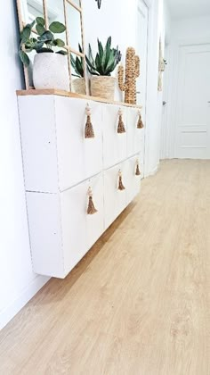 a hallway with white cabinets and plants on the top shelf, along with wooden flooring