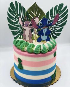 a birthday cake decorated with two cartoon characters on top of it and palm leaves around the edges