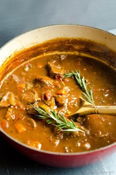 a red pot filled with stew on top of a table next to a wooden spoon