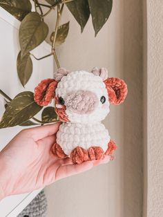 a hand holding a small crocheted animal next to a potted plant