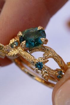 a close up of a person's hand holding a gold ring with green and blue stones