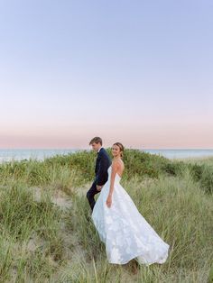 a bride and groom walking through the sand dunes at sunset