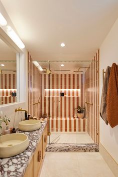 a bathroom with two sinks and striped wallpaper in the shower area, along with a large mirror