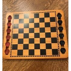 a wooden chess board with black and red pieces on it, sitting on a wood floor