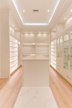 an empty walk in closet filled with white shelves and glass cases on either side of the room