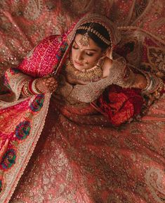 a woman in a red and gold wedding outfit sitting on a bed with her hands together