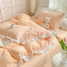 a bed with pink sheets and white ruffles on it, next to a vase filled with tulips