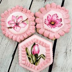 three cupcakes decorated with pink flowers on top of a wooden table next to each other