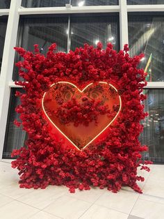 a heart - shaped sculpture made out of red flowers in front of a building window