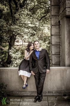 a man and woman standing next to each other in front of some trees with their arms around each other