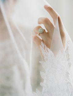 a close up of a person wearing a wedding ring on their finger and veil over her face