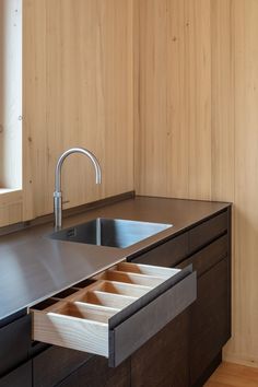 a kitchen sink with drawers underneath it in front of a counter top and wooden paneled walls