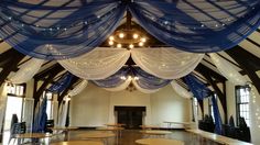 the inside of a building with tables and blue drapes hanging from it's ceiling