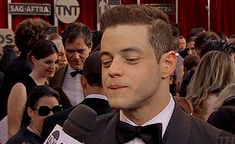 a man in a tuxedo and bow tie is talking to the media at an event