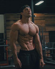 a shirtless man standing in a gym with his hands on his hips and looking up