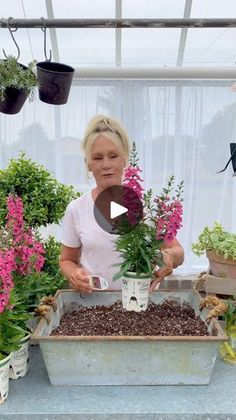 a woman is working in a greenhouse with potted plants and flowers on the table