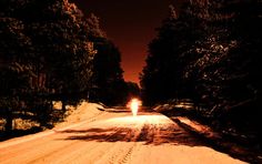 a car driving down a snow covered road in the woods at night with its headlights on