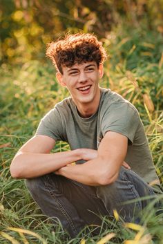 a young man is sitting in the grass with his arms crossed and looking at the camera