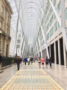 many people are walking down the walkway in an indoor shopping mall with glass ceilinging