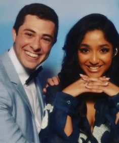 a man and woman posing for a photo in front of a blue background with their arms around each other