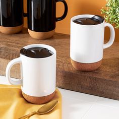 two coffee mugs sitting on top of a wooden table next to a potted plant