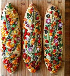 three different types of bread on a cutting board with tomatoes, onions, and other veggies