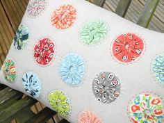 a pillow with many different colored flowers on the front and back of it, sitting on a wooden bench