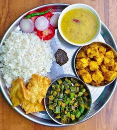 a metal plate topped with different types of food on top of a wooden table next to rice