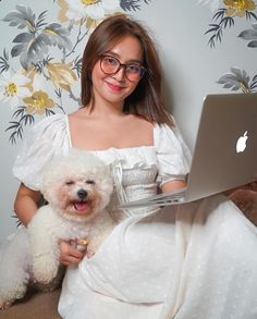 a woman in a white dress holding a dog and using a laptop