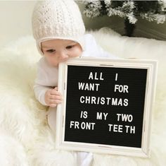 a baby holding up a sign that says all i want for christmas is my two front teeth