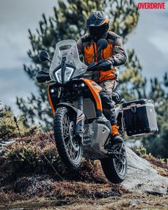 a man riding on the back of an orange and black motorcycle down a dirt road