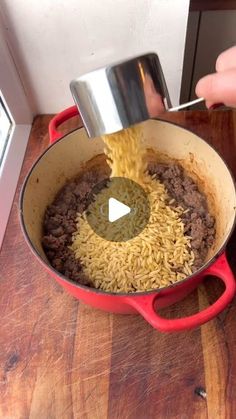 someone is pouring rice into a pot with meat and vegetables in it on a wooden table