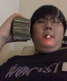 a man with glasses is holding a stack of money in his hand and looking at the camera