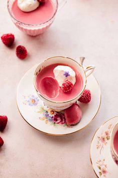 two cups filled with raspberries and cream on top of saucers next to each other