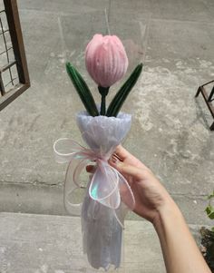 a hand holding a plastic bag with two flowers in it and a ribbon tied around the end