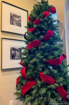 a christmas tree decorated with red ribbon and bows in front of two framed pictures on the wall