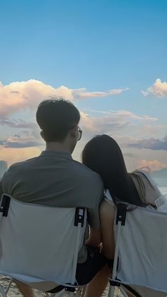 two people sitting in lawn chairs facing the ocean with their backs to each other looking at the sky