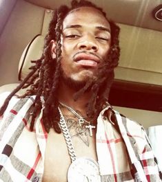 a man with dreadlocks sitting in the back seat of a car wearing a checkered shirt