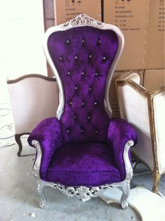 a purple chair sitting on top of a floor next to a box and some chairs